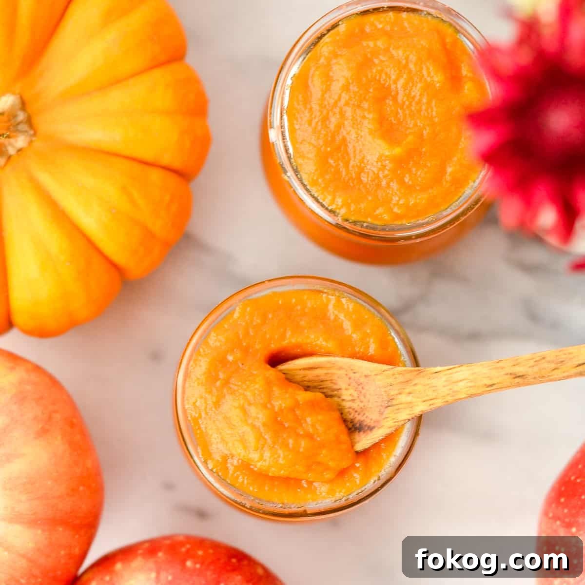 Overhead view of a spoon scooping out some Homemade Apple & Pumpkin Baby Food from a glass jar