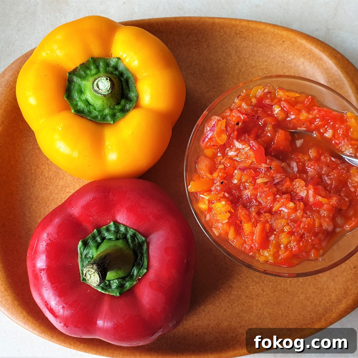 A red pepper and yellow pepper along side a dish of sweet pepper relish.