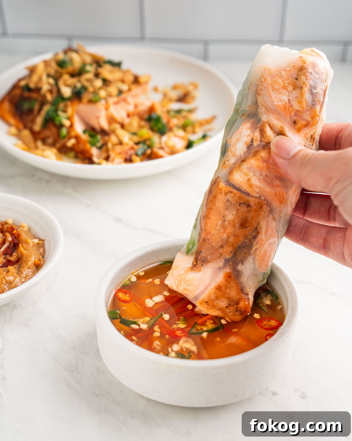 hand dipping salmon spring roll into fish sauce dip.