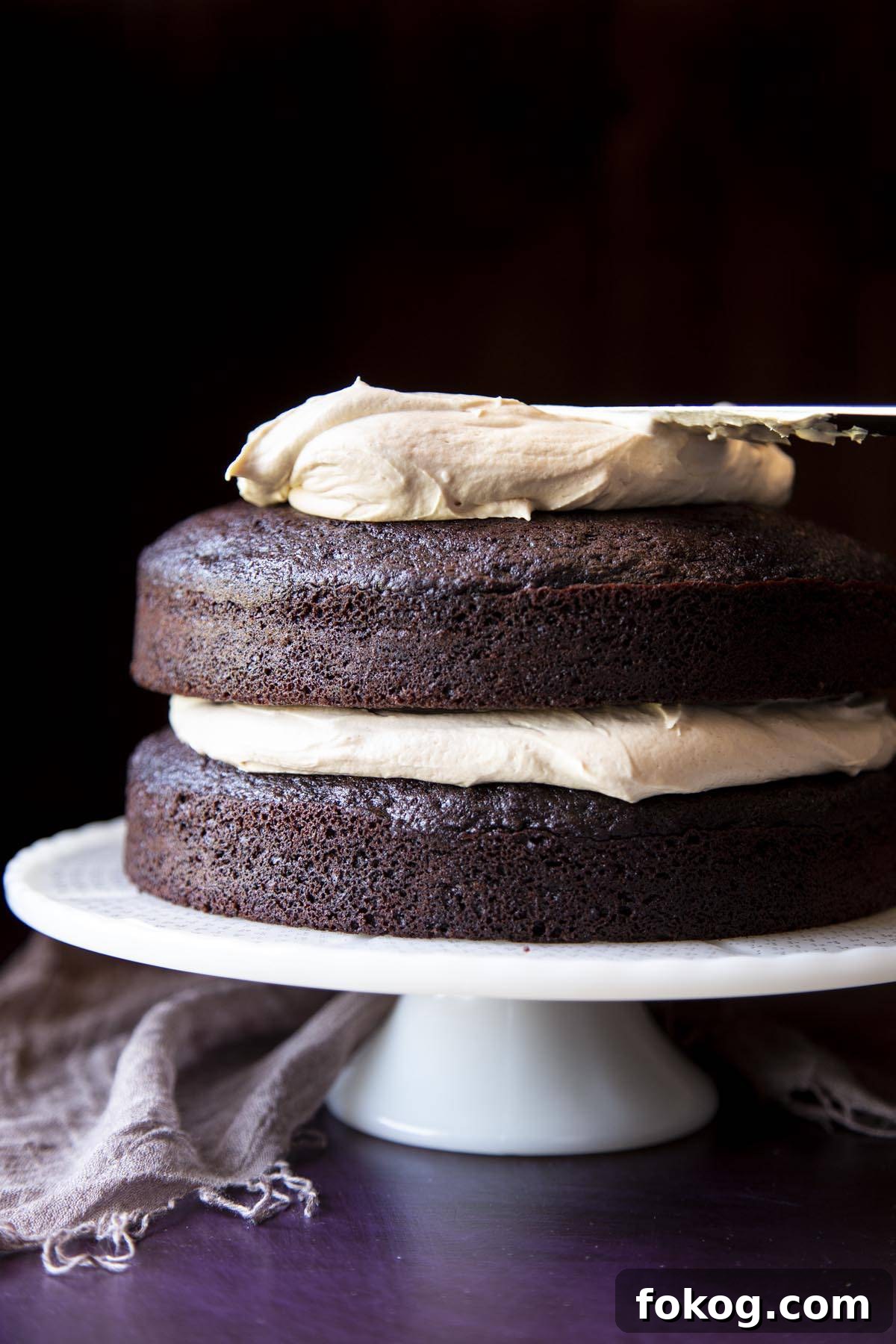 Peanut butter frosting is being spread on top of a two layer chocolate cake