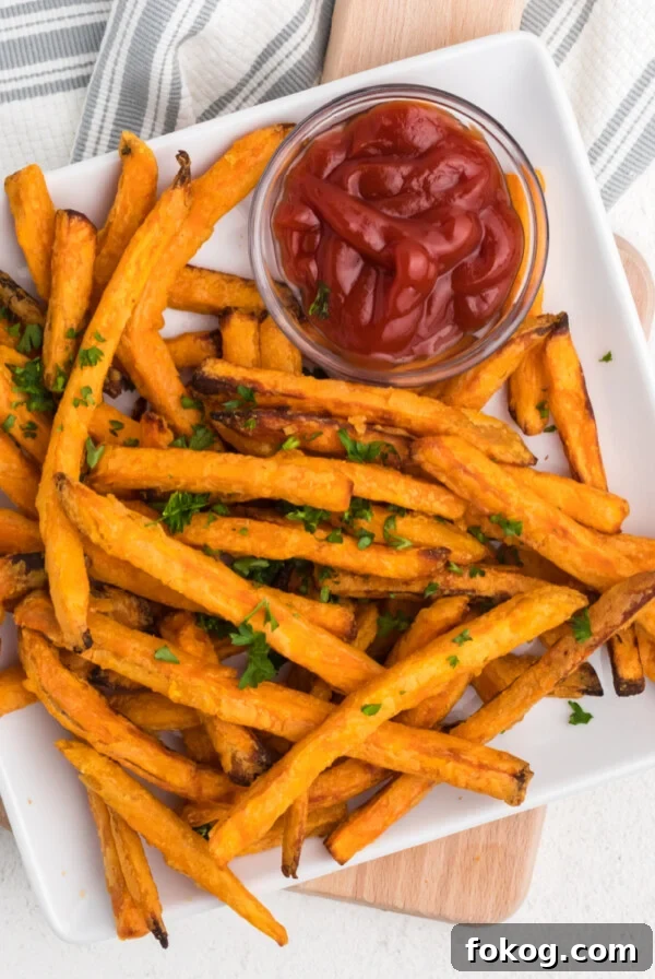 Frozen sweet potato fries made in the air fryer - fully cooked and served on a white plate with a side of ketchup.