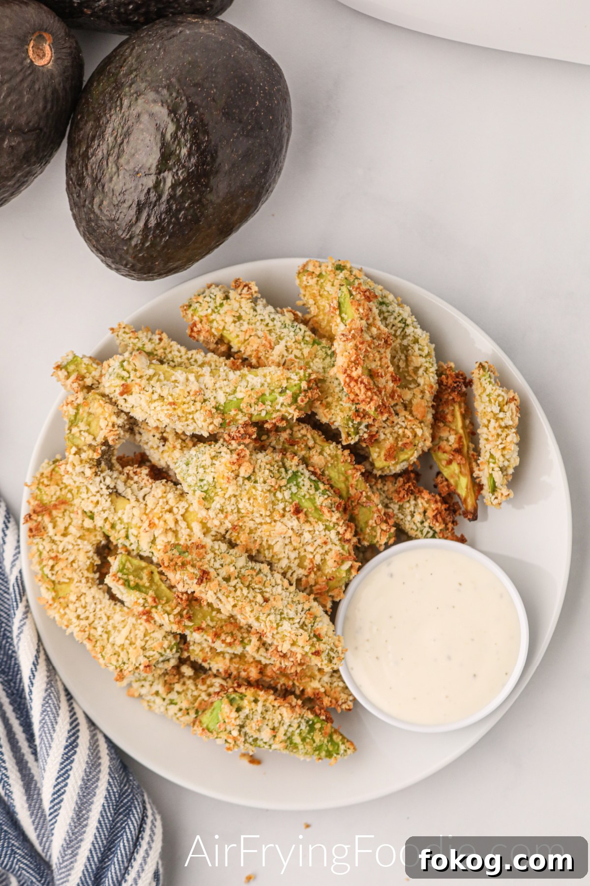 Overhead shot of air fryer avocado fries on a plate with dipping sauce and avocados off to the side.