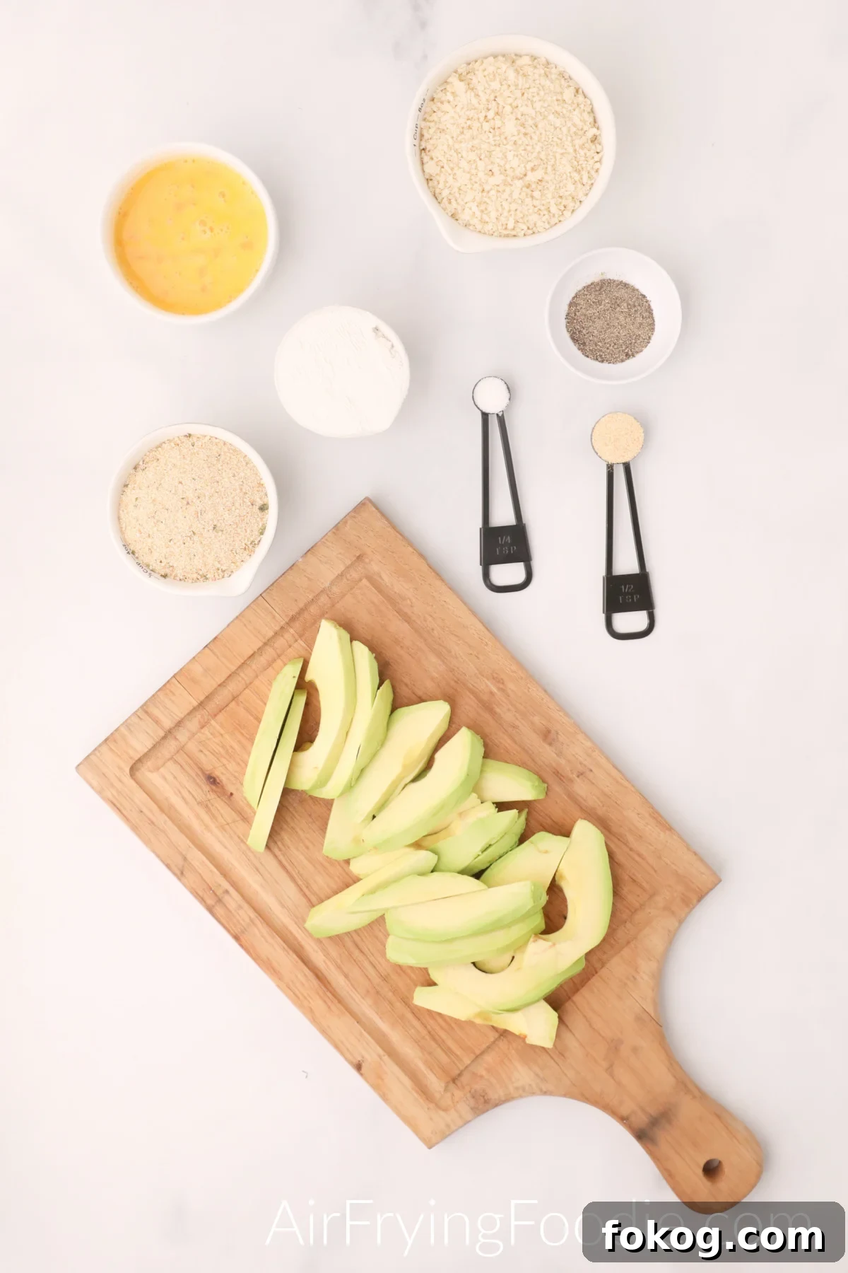 avocado sliced on a cutting board and ingredients on a white table top.