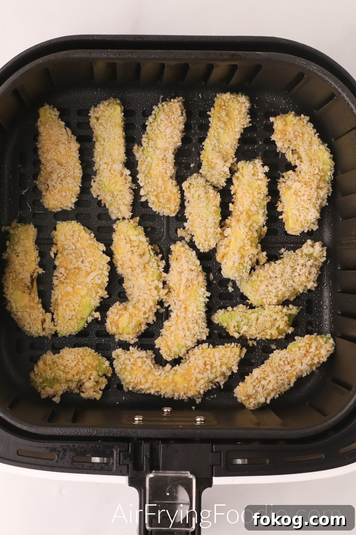 Avocado fries in the basket of the air fryer ready to be cooked.