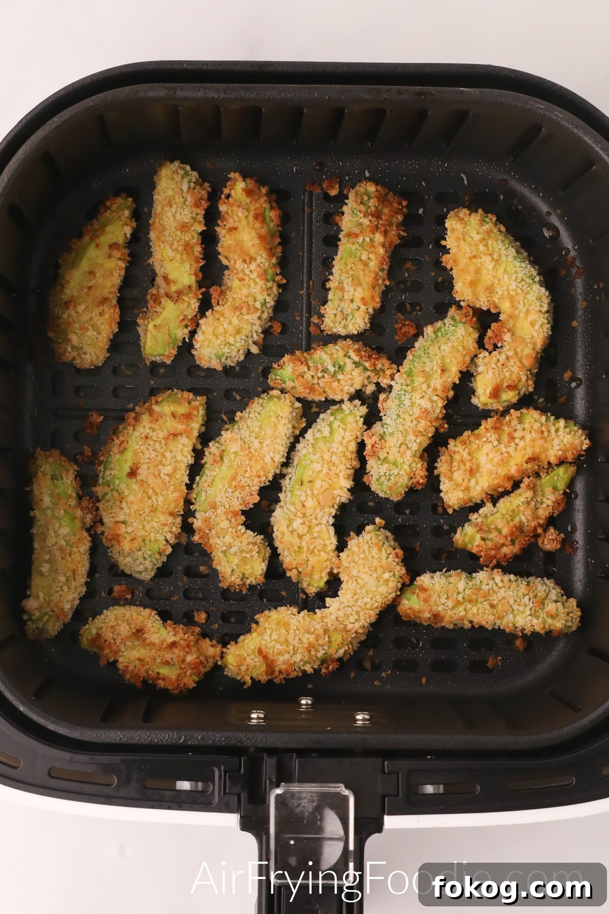 Avocado fries in the basket of the air fryer, fully cooked and ready to serve.