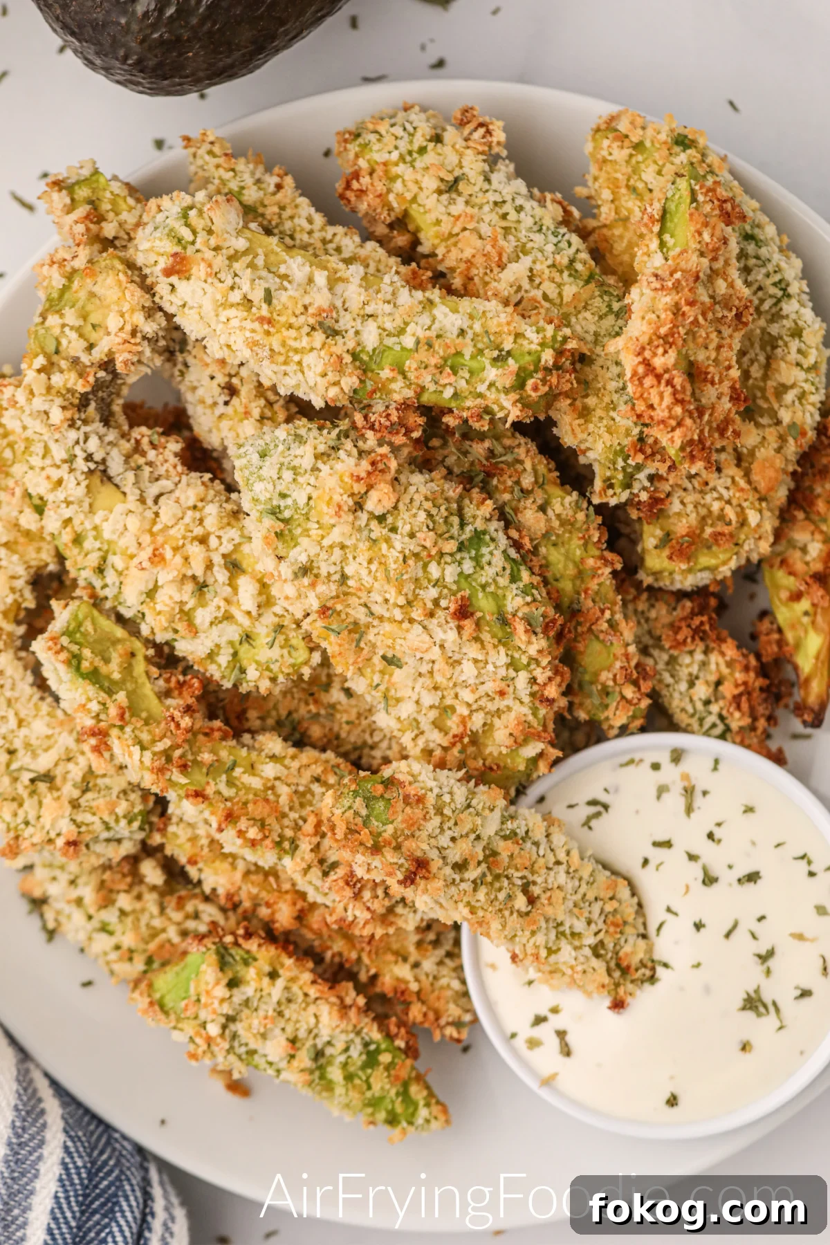 Air fryer avocado fried served on a white plate with dipping sauce.