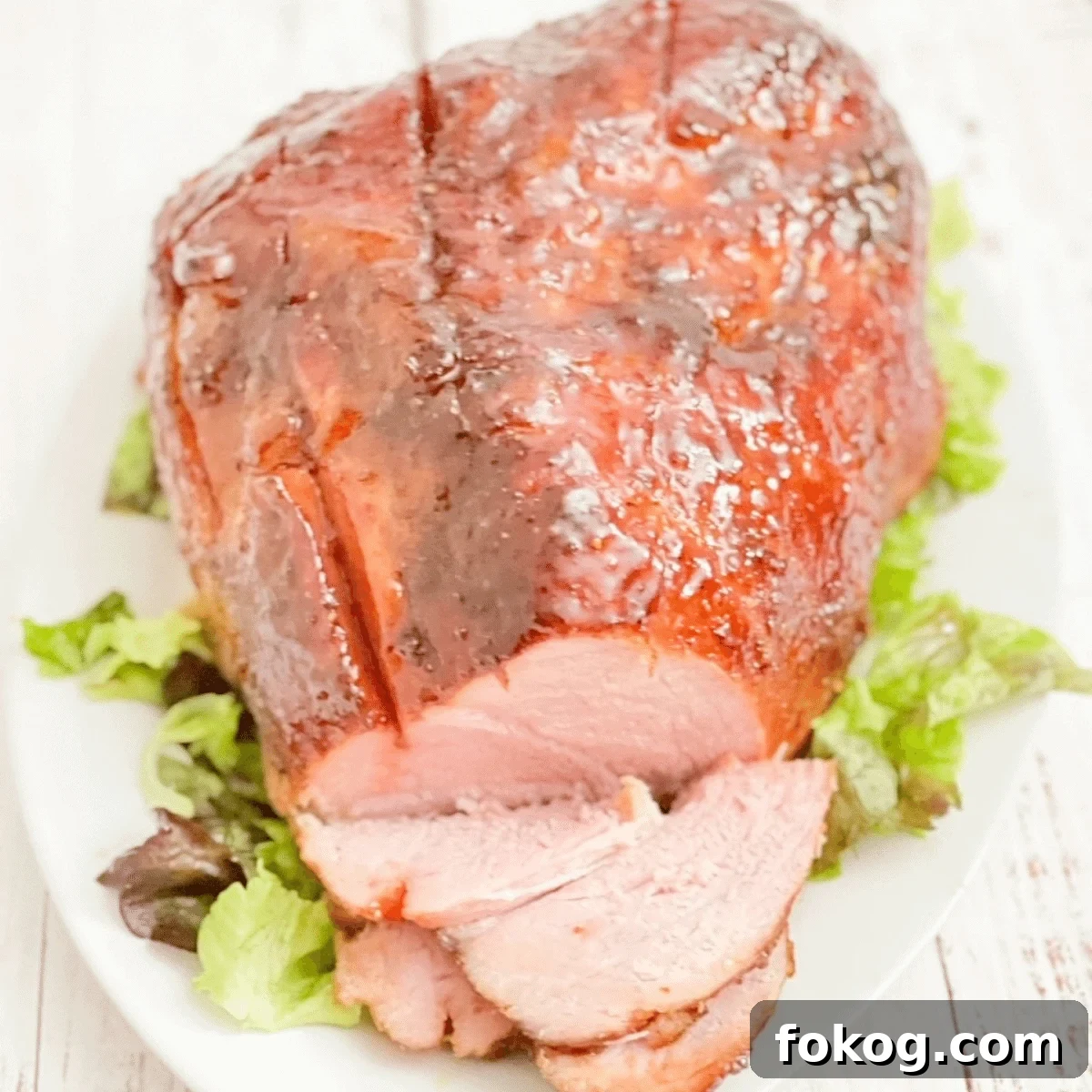 Double smoked ham on white platter, covered in glaze, with green lettuce for garnish.