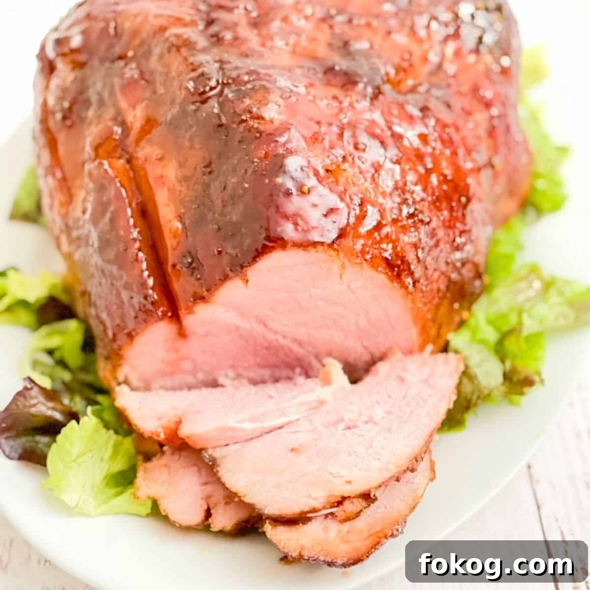 Twice smoked ham on a white platter with lettuce leaves underneath, with a few pieces sliced off the ham.