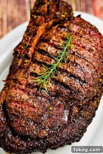 Smoked prime rib roast on white serving platter, with a sprig of rosemary on top.