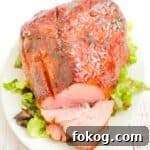 A double smoked ham on a white serving platter, a few pieces sliced, sitting on top of green lettuce.