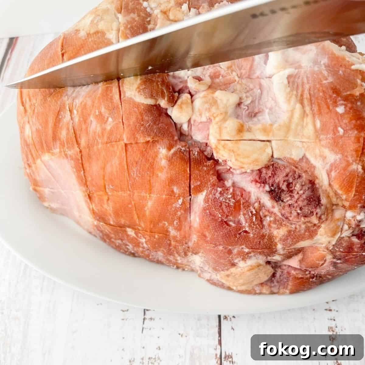 A sharp knife scoring the outside of the ham.