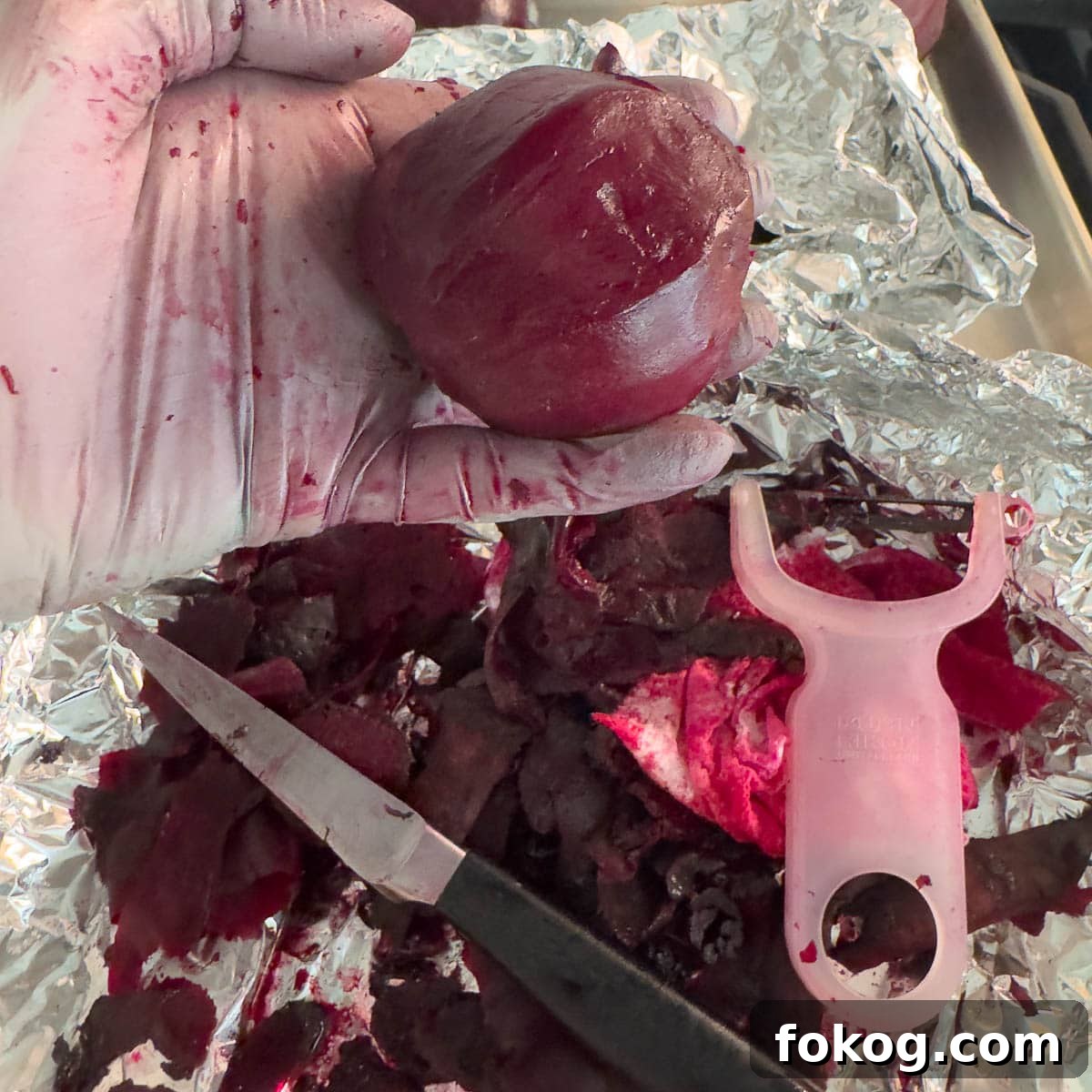 A gloved hand holding a peeled red beet with a paring knife and a y-vegetable peeler.