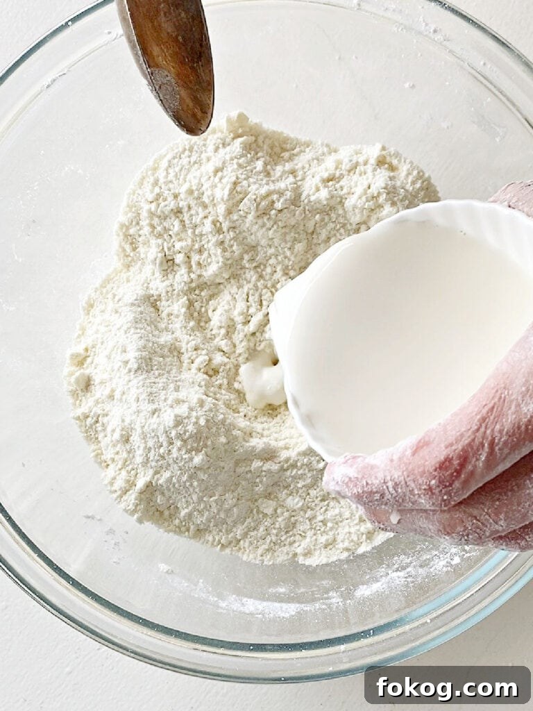 Pouring milk into flour mixture in a glass bowl. White background. 
