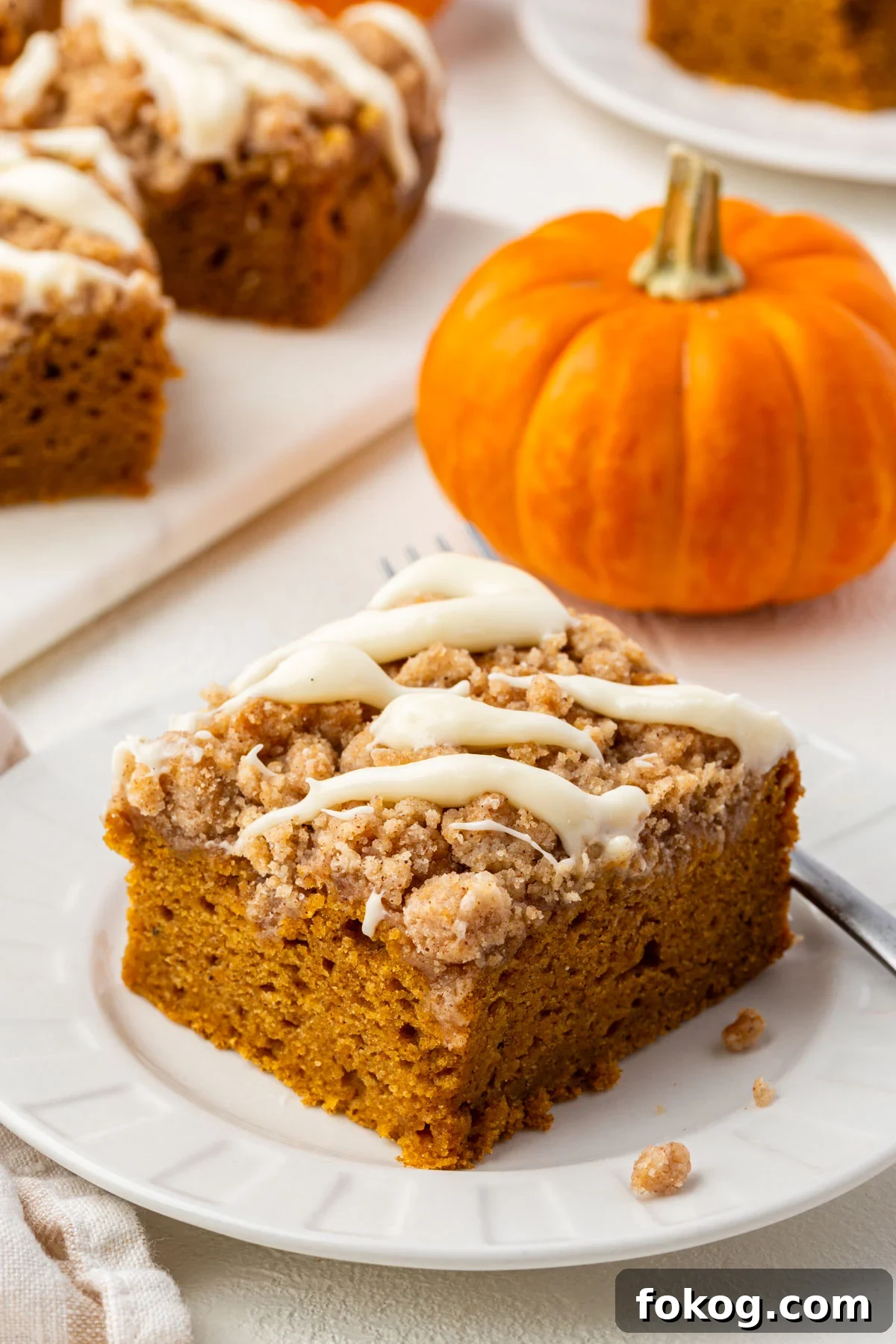 Close-up of a single slice of gluten-free pumpkin coffee cake with streusel topping and cream cheese glaze beside a fork.