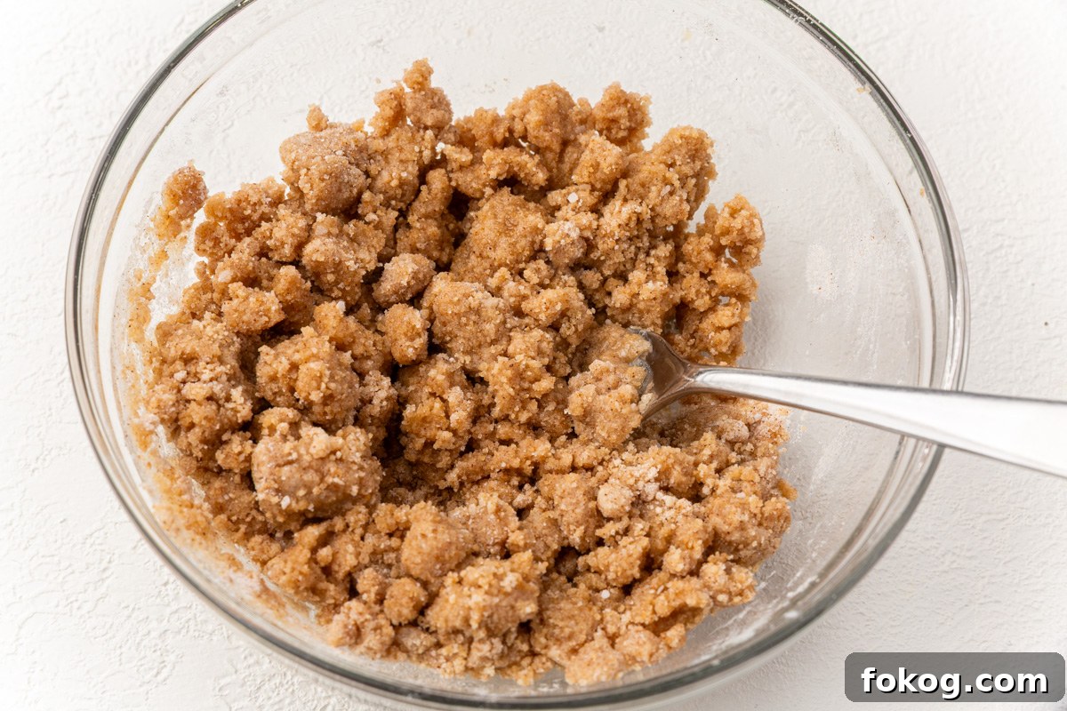 Cinnamon streusel topping mixture in a bowl with a spoon, ready to sprinkle over pumpkin coffee cake.