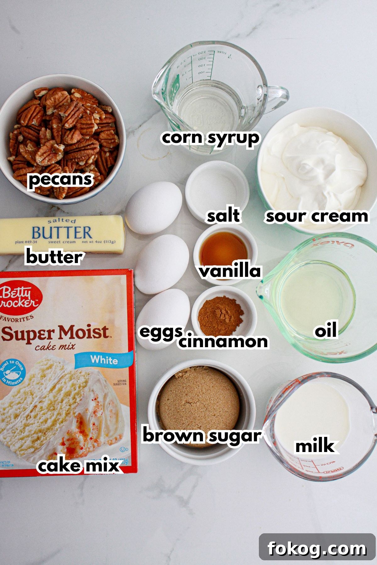 pecans, butter, cake mix, corn syrup, salt, vanilla, cinnamon, eggs, brown sugar, sour cream, oil and milk on a counter.