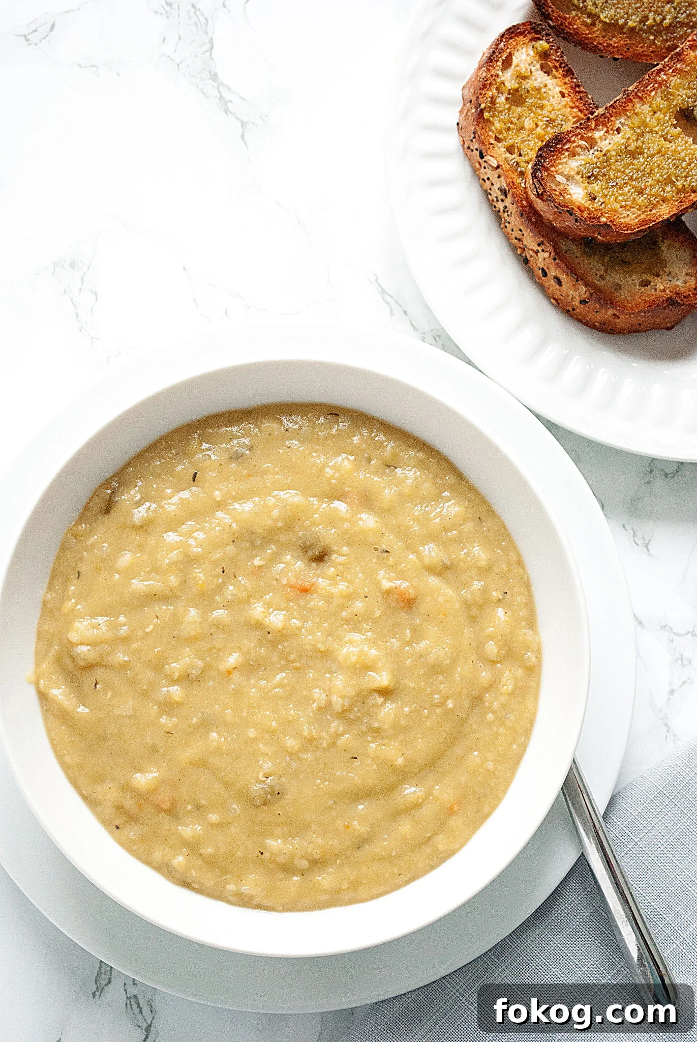 a bowl of split pea soup and a plate of toasted bread on a table