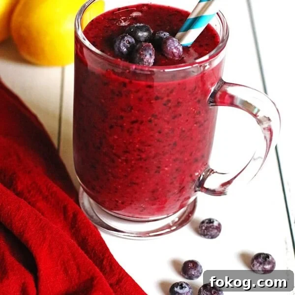Smoothie made with blueberries and lemon in a clear mug sitting on a white table.