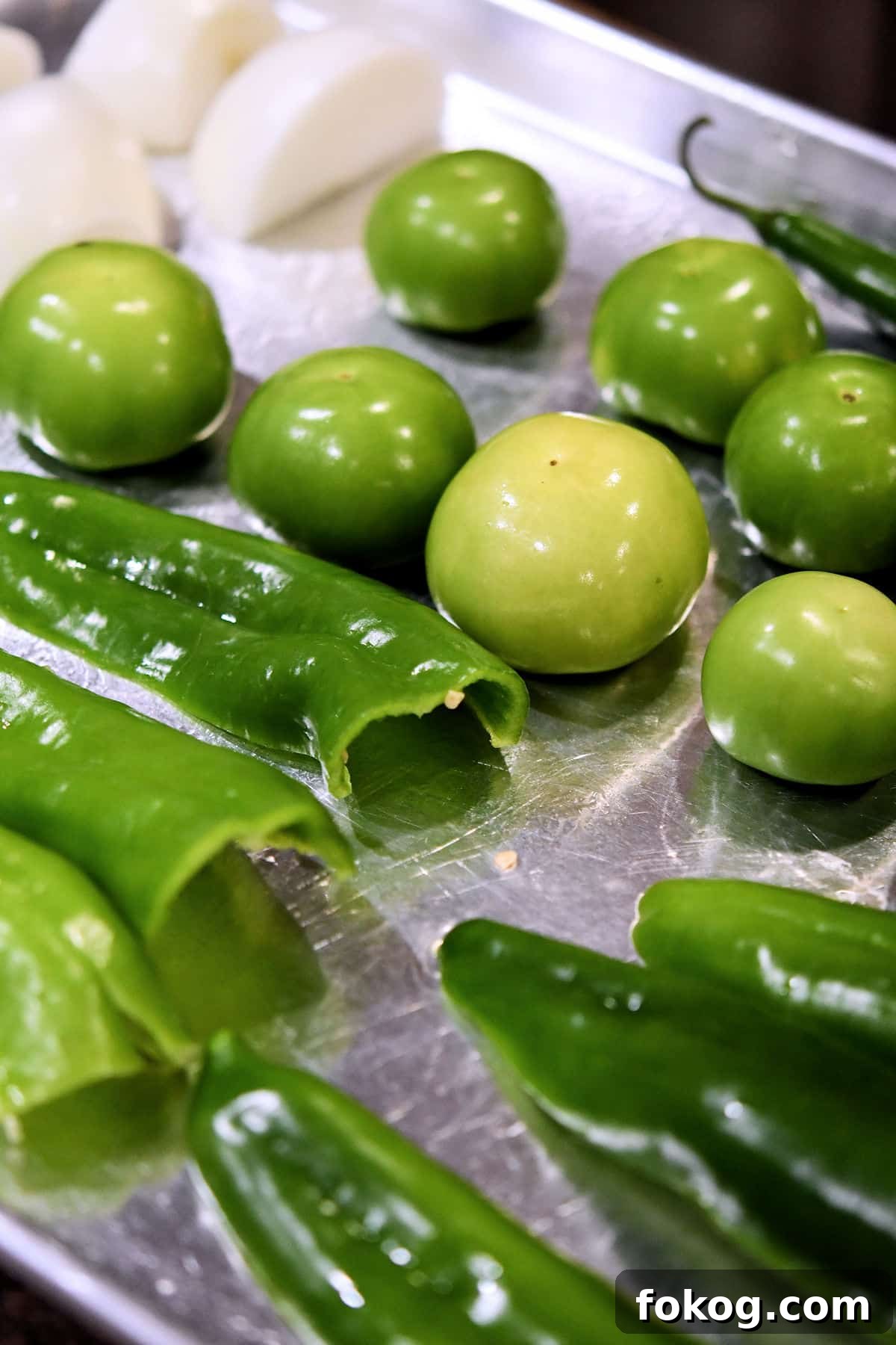 Chile Verde Pork Guisado Recipe 5 Anaheim chiles and tomatillos on a baking sheet, ready for broiling in the oven
