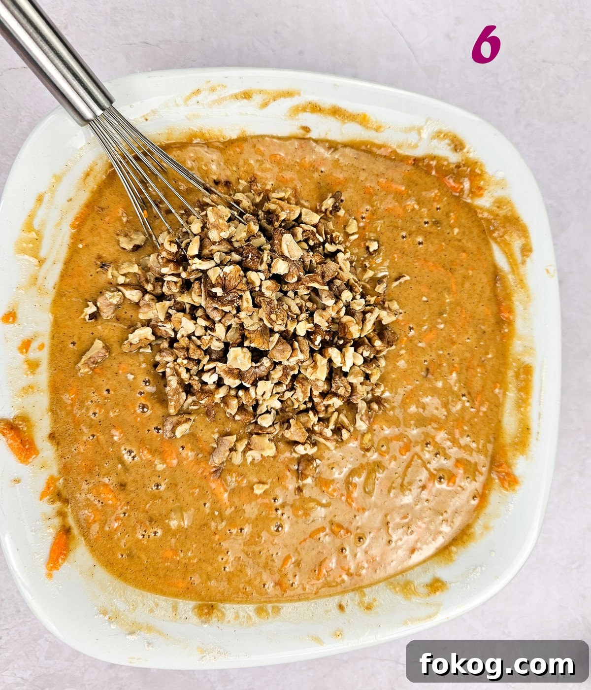 Roasted walnuts in carrot cake batter in a mixing bowl.