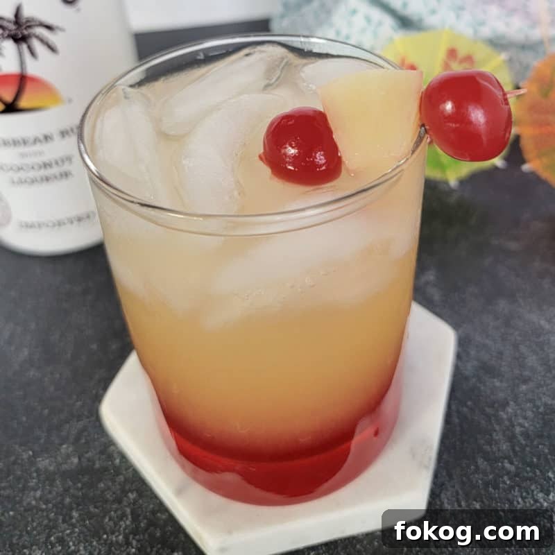 24+ Tropical Pineapple Juice Cocktail Recipes 11 Malibu sunset drink in a clear glass garnished with maraschino cherries and pineapple chunk