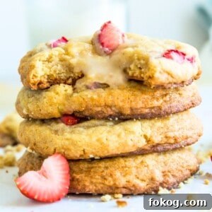 A stack of strawberry cheesecake cookies with fresh strawberries around them.