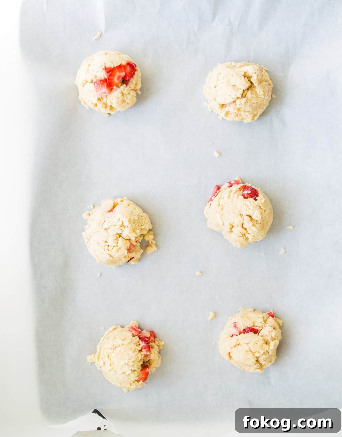 A baking sheet with strawberry cookie dough balls on it.