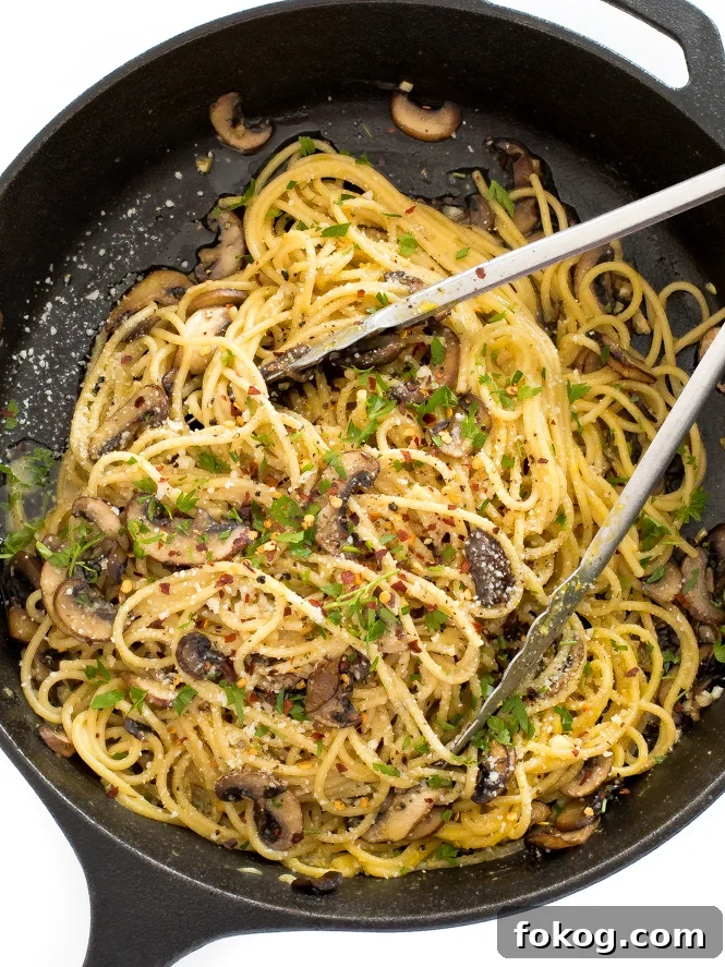 Top view of noodles with mushrooms in a pan with tongs. 