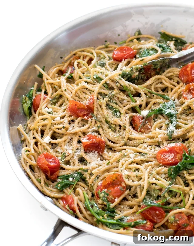 Pasta in a silver pan with tomatoes and basil and tongs. 