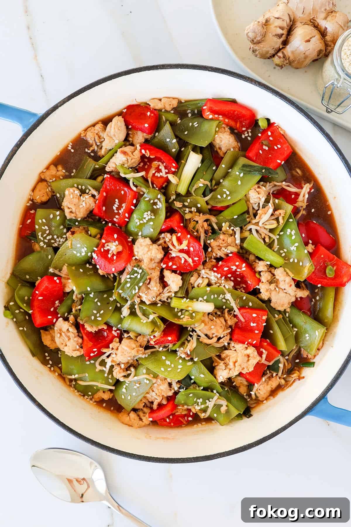 Ground chicken stir fry with veggies in a skillet with spoon on the bottom.