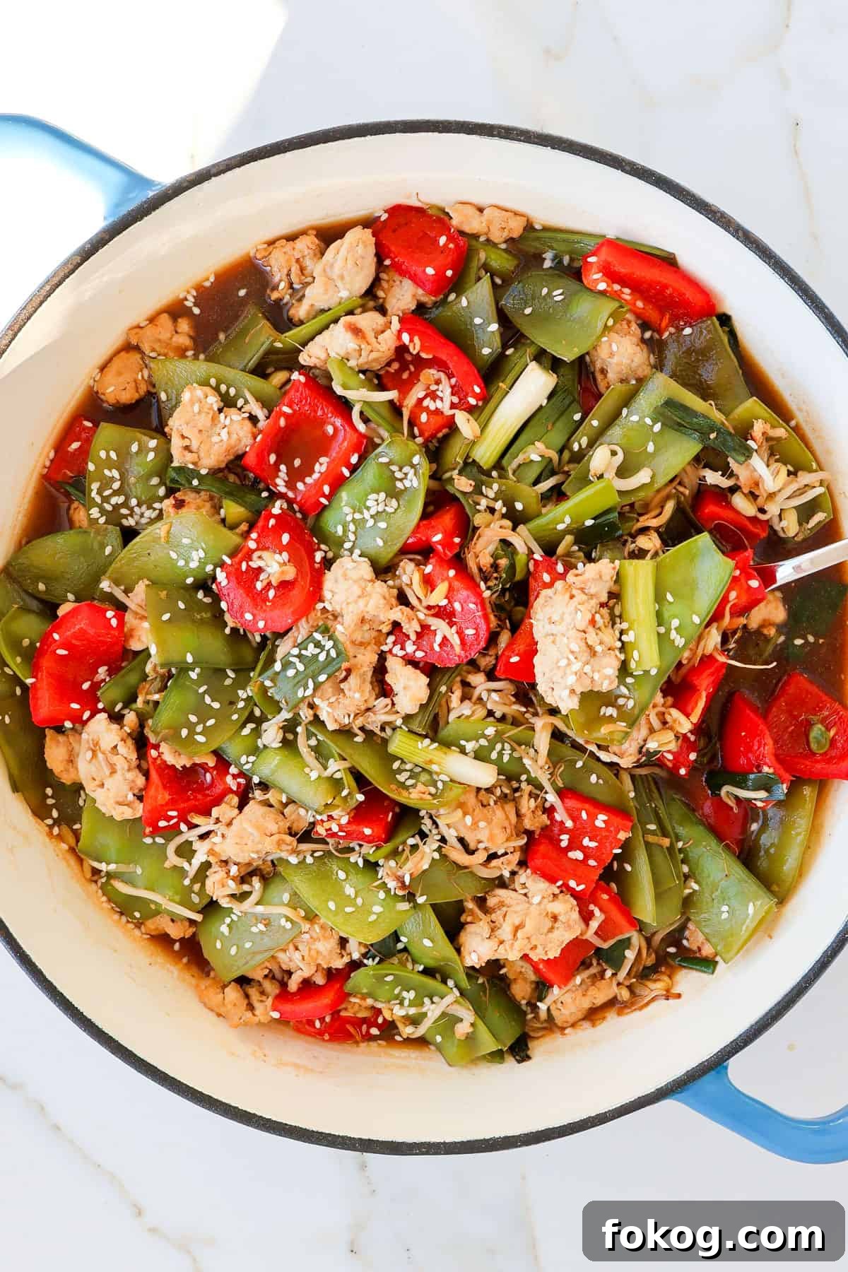 Chicken stir fry in a skillet with a spoon.